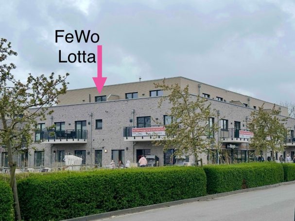 Moderne Wohnanlage mit der Beschriftung "FeWo Lotta" und grüner Bepflanzung.